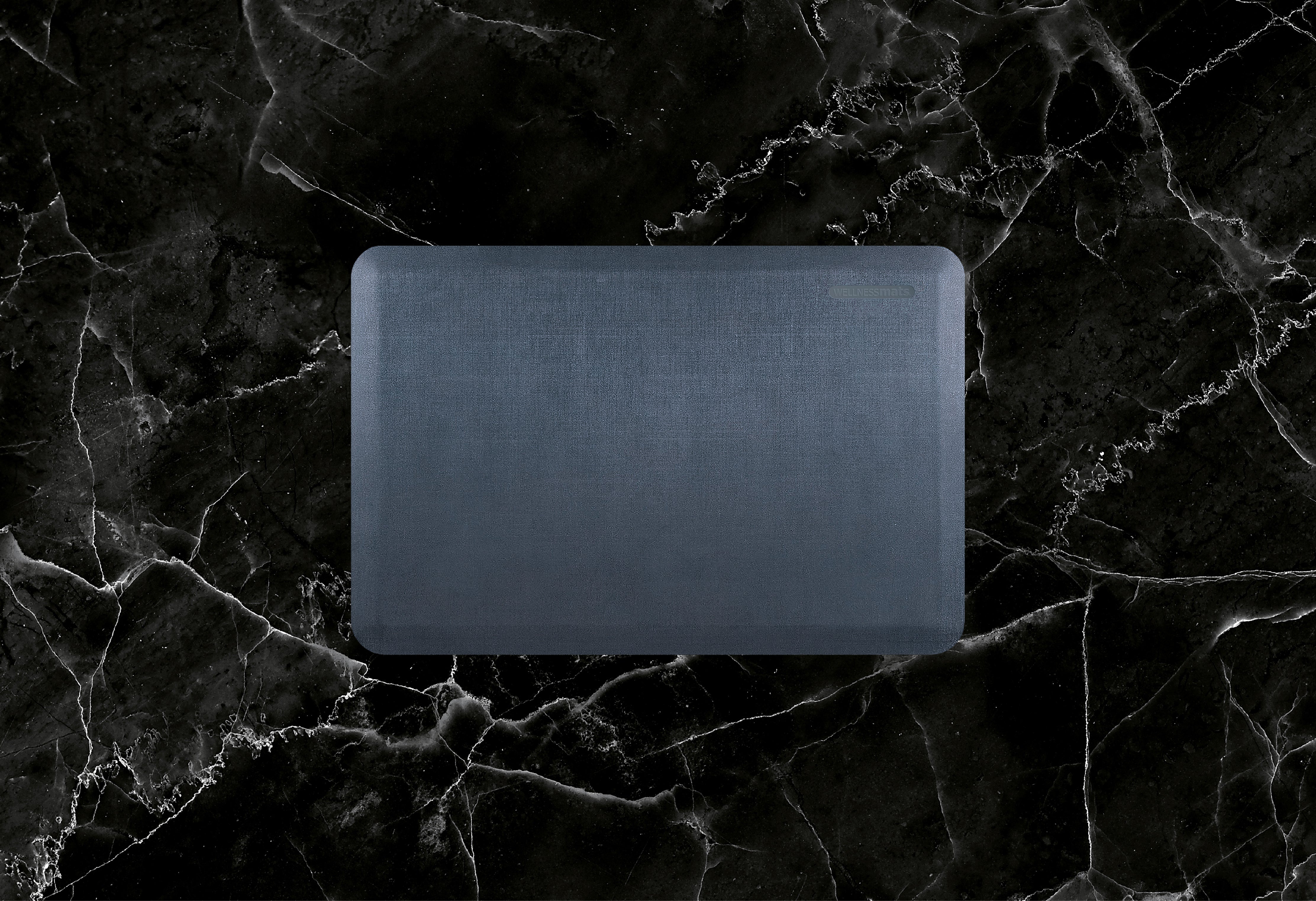 A 3'x2' Linen Lagoon WellnessMat on a black marble floor.