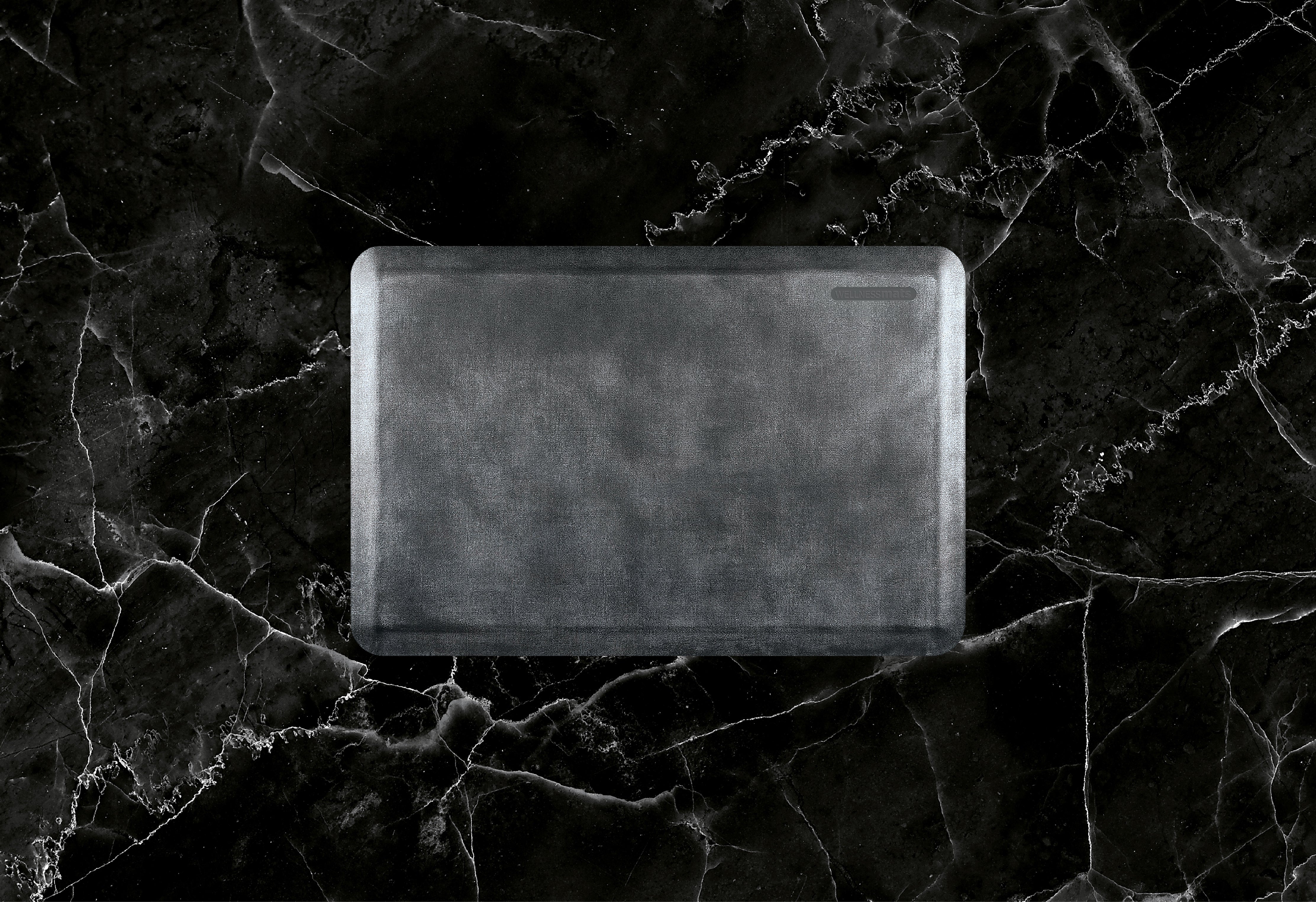 A 3'x2' Linen Onyx WellnessMat on a black marble floor.