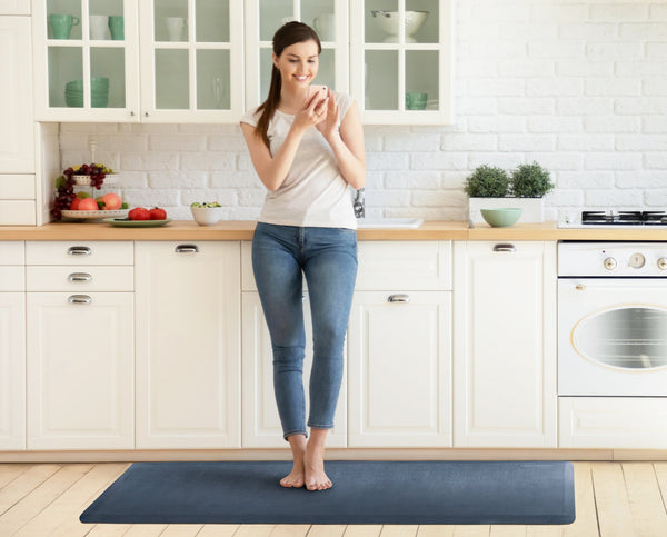 A woman standing on a 6'x2' lagoon WellnessMat in a kitchen.