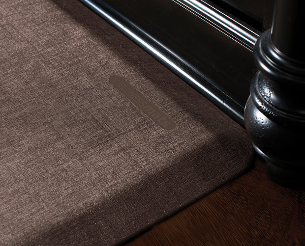An up-close shot of a 3'x2' Antique Dark WellnessMat in front of a dark wood vanity.