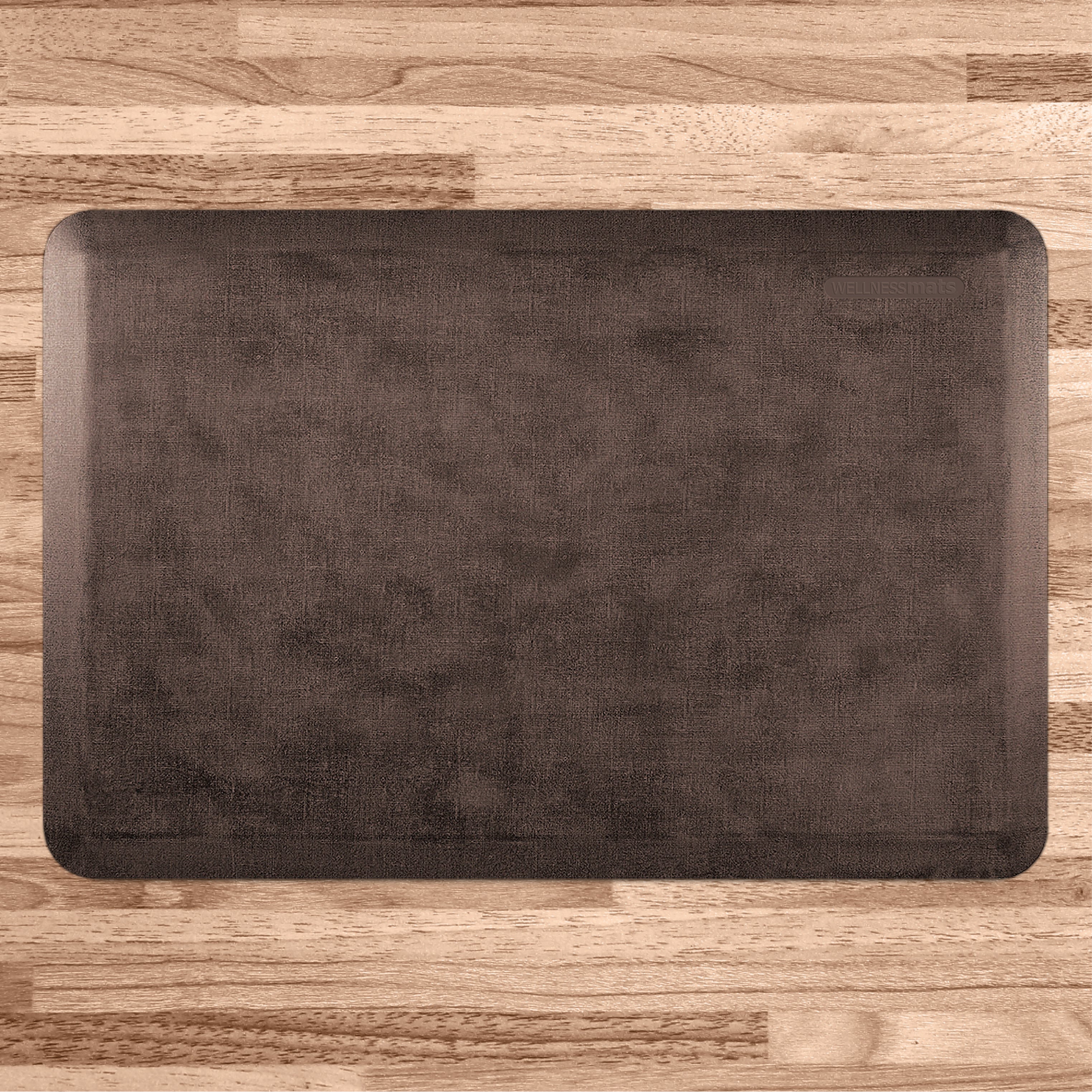 A 3'x2' Antique Dark WellnessMat on a light wood floor.