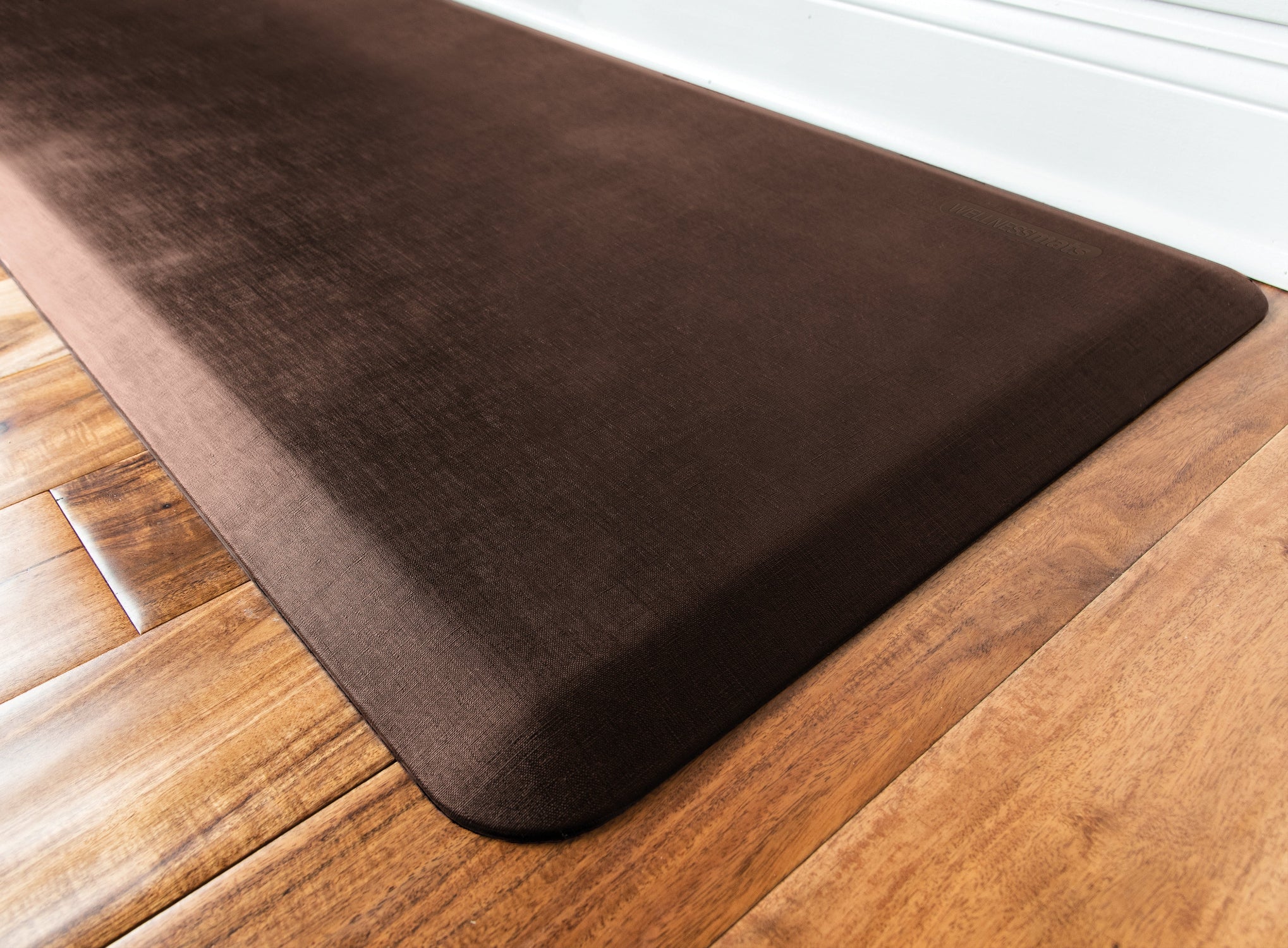 An up-close shot of a 6'x2' Antique Dark WellnessMat on a light wood floor.
