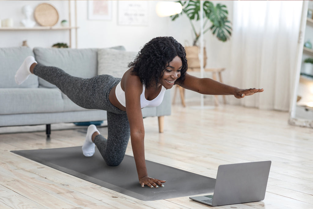 Woman doing yoga on Fitnessmat in front of laptop