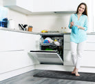 A woman standing on a 6'x2' Linen Onyx WellnessMat while doing dishes. 