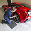 Man kneeling on a MobileMat while cleaning the wheel of a red sports car in a garage setting.